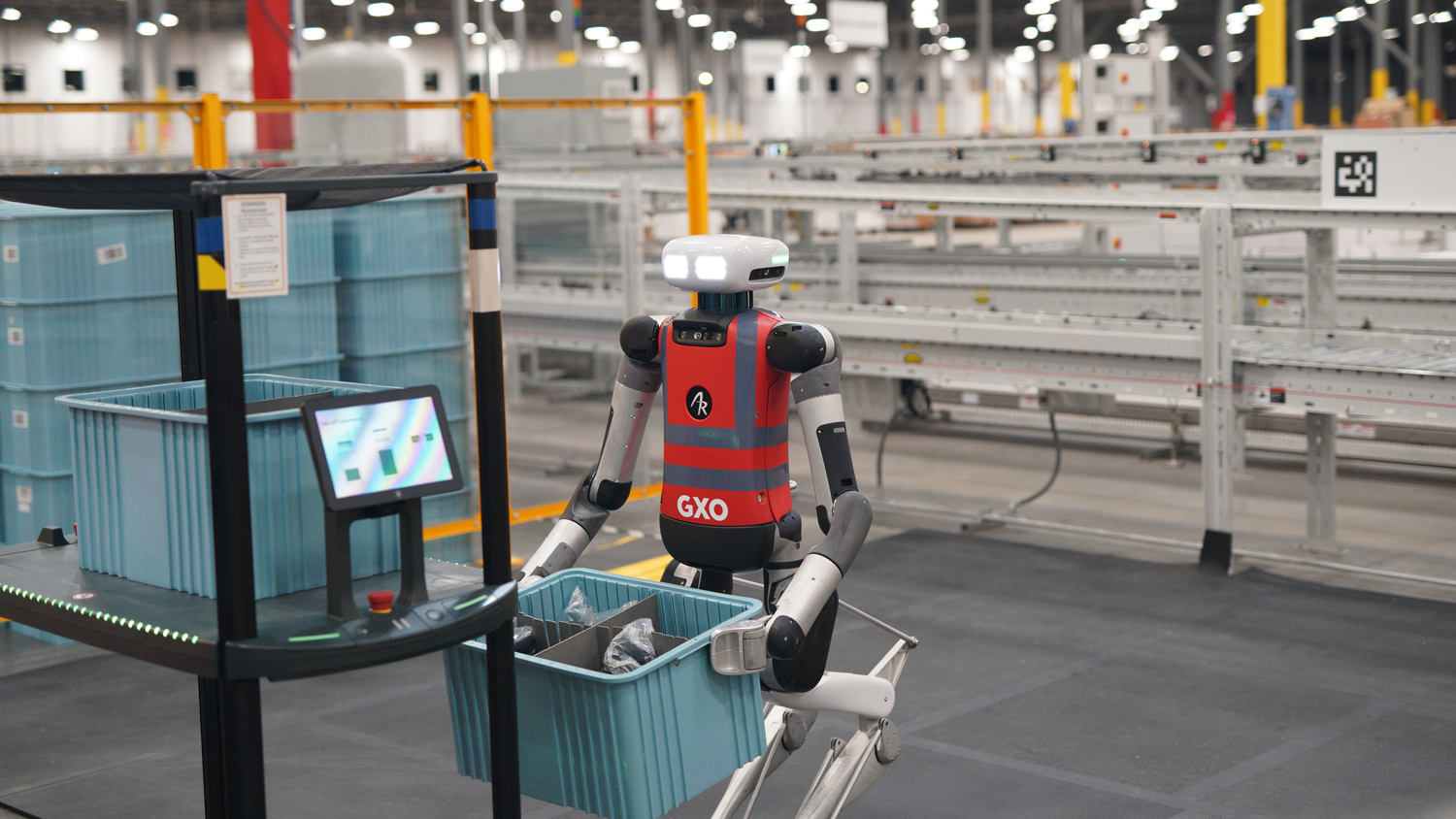 Agility Robotics Digit humanoid handling a tote beside warehouse automation in a GXO commercial deployment